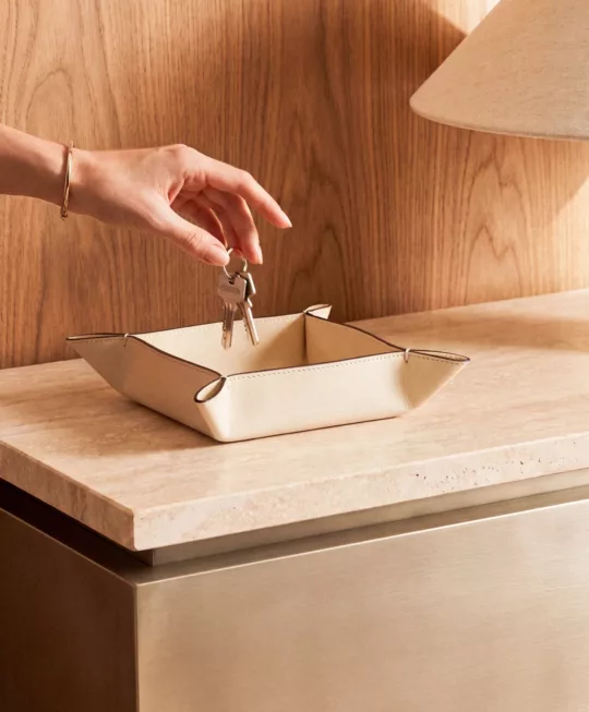 A hand places keys in a pale leather tray.