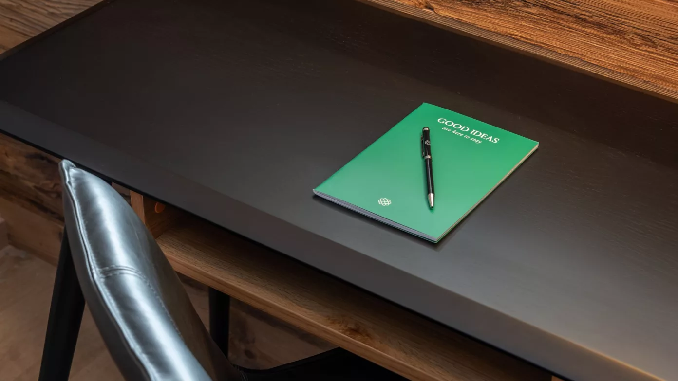 A green Emerald Stay notebook and a pen on a black wooden desk.
