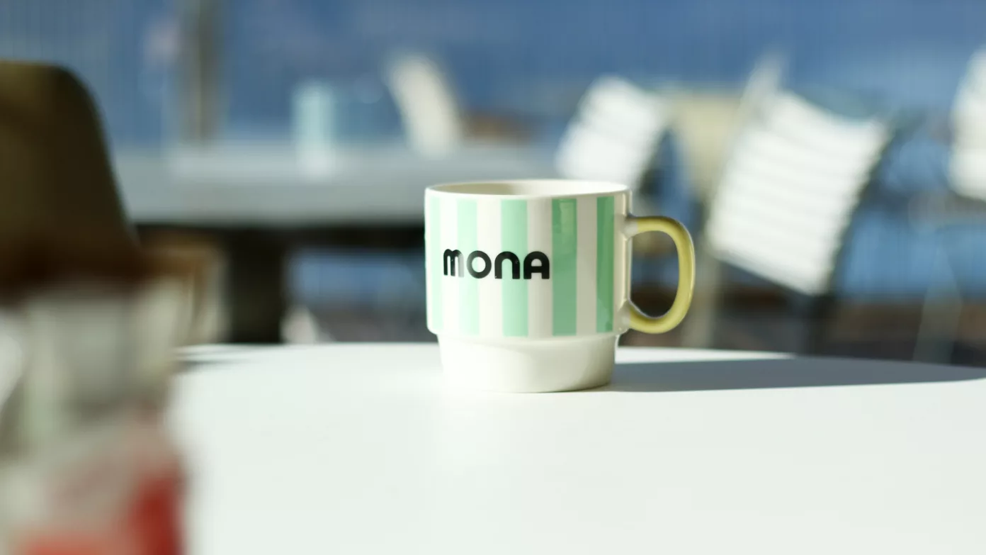 A mint-striped MONA mug on a terrace table by the lake.