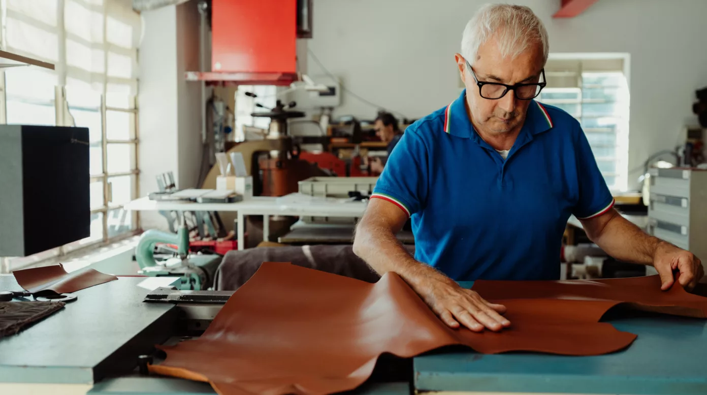 In a workshop, a craftsman smooths a large cognac leather hide by hand.