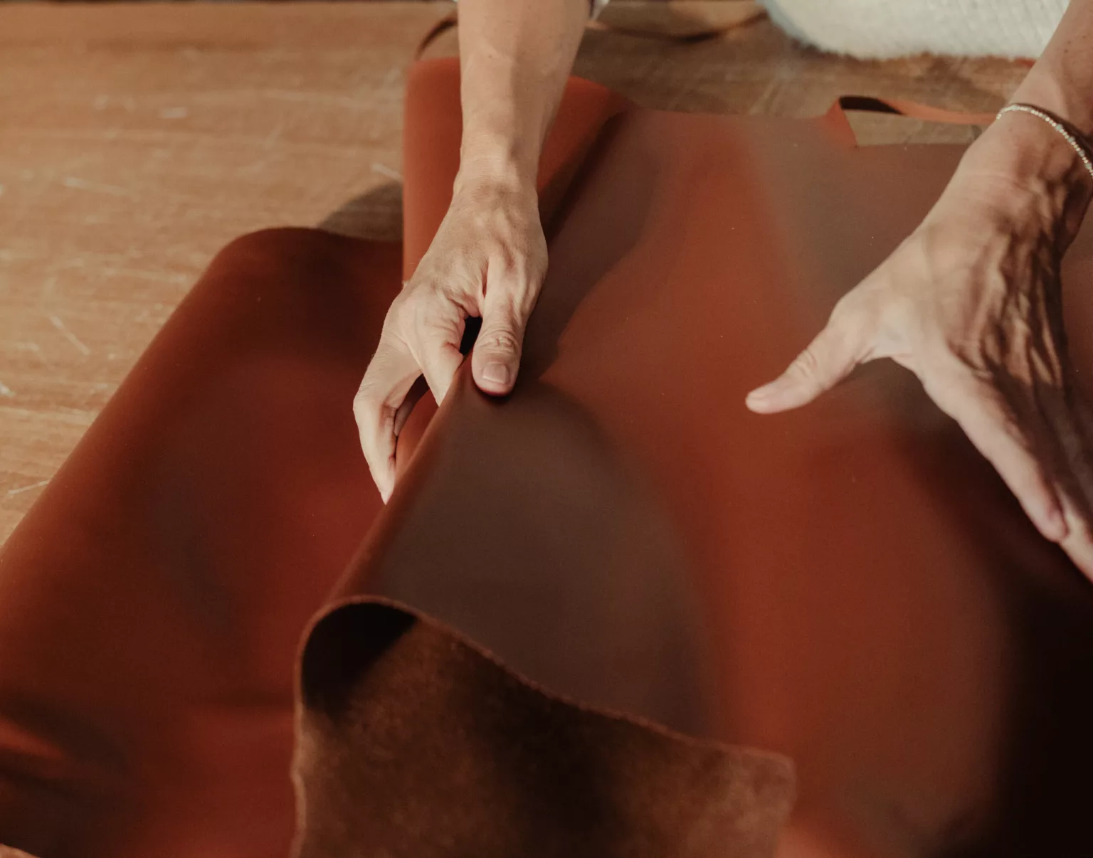 Deux mains déroulent une grande peau de cuir brun sur un plancher de bois.
