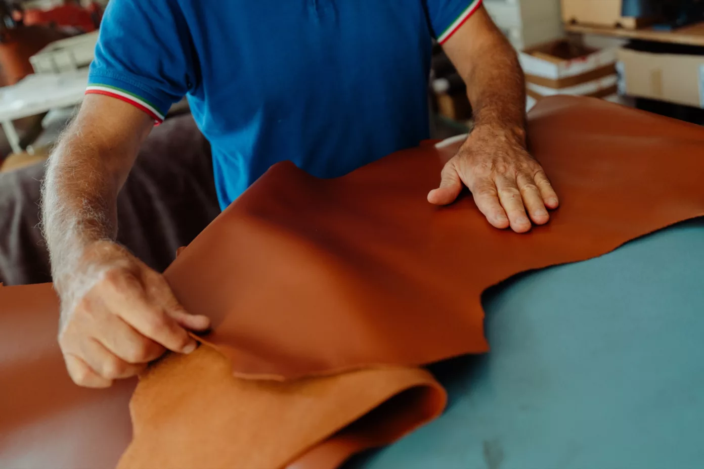A craftsman smooths a tan leather hide by hand on his workbench.