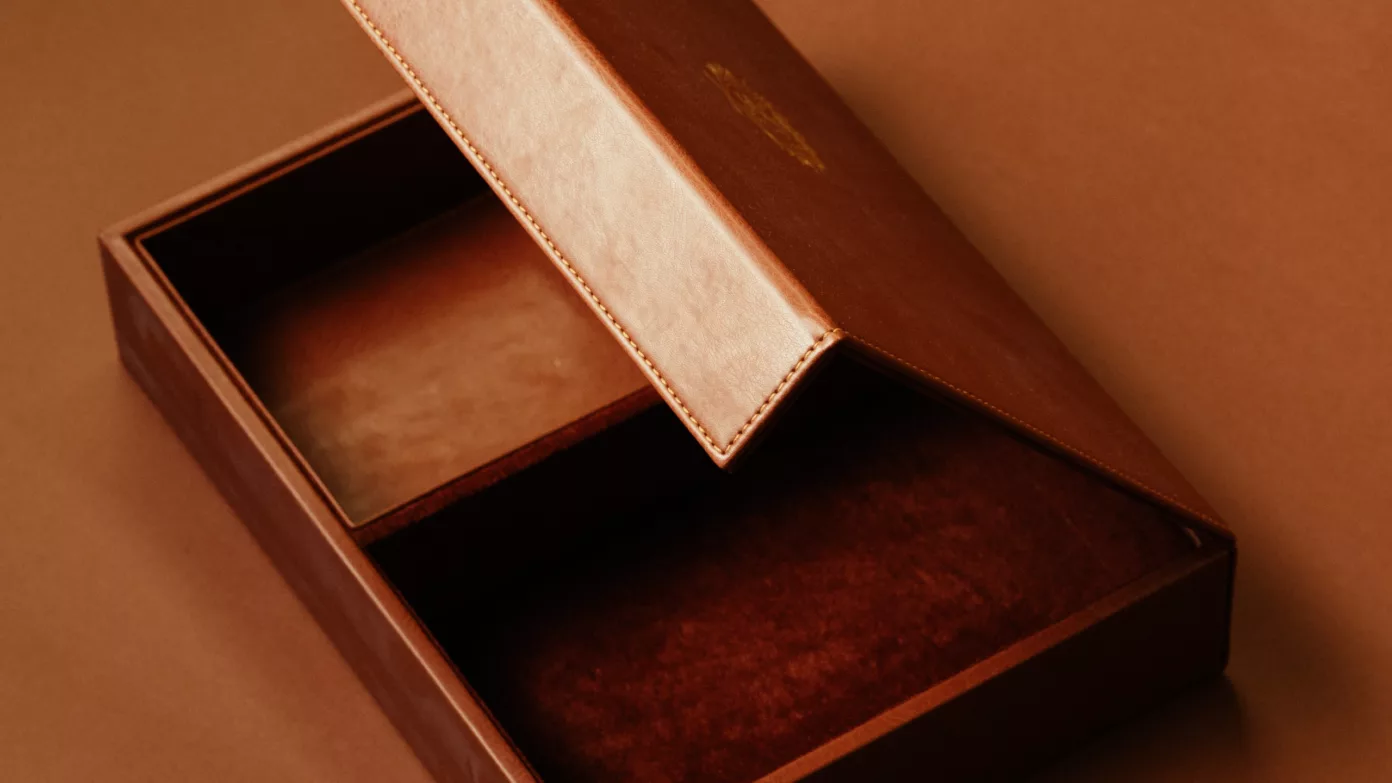 Un coffret gainé de cuir cognac, au couvercle surpiqué entrouvert sur un intérieur de velours.