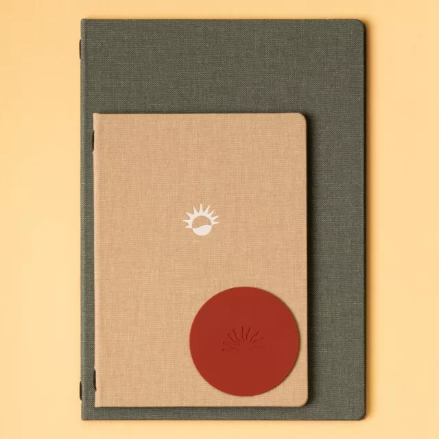 Carnets reliés en toile vert-de-gris et sable à reliure à vis, sous-verre en cuir rouge embossé d’un soleil