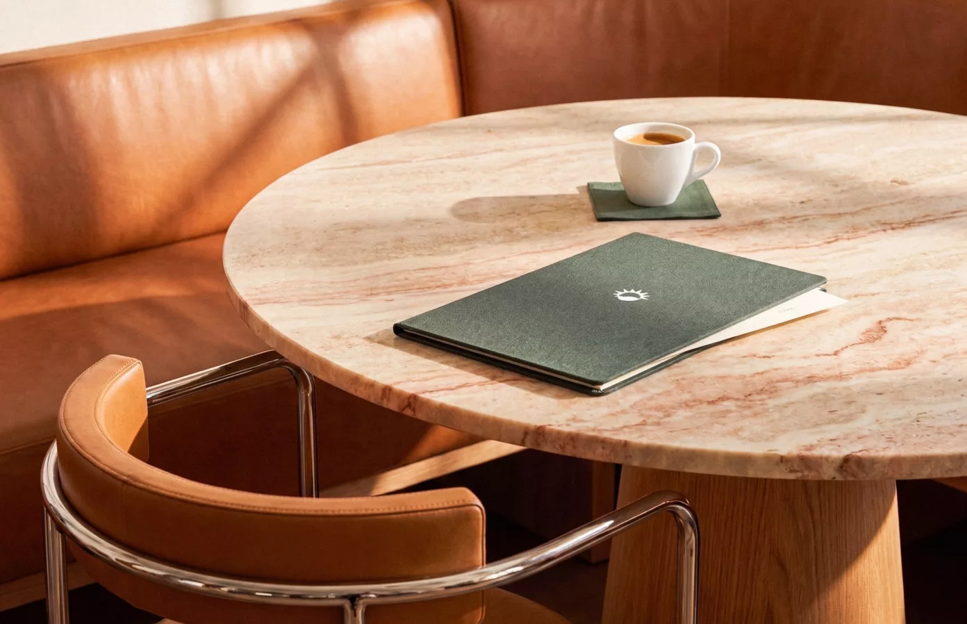 Porte-menu vert et sous-verre assorti sur une table en marbre, banquette et fauteuil en cuir cognac, accessoires de table sur-mesure, Maison Maëstra
