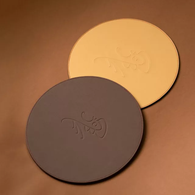 Sous-assiettes rondes en cuir jaune et chocolat embossées d’un monogramme, accessoires de table sur-mesure