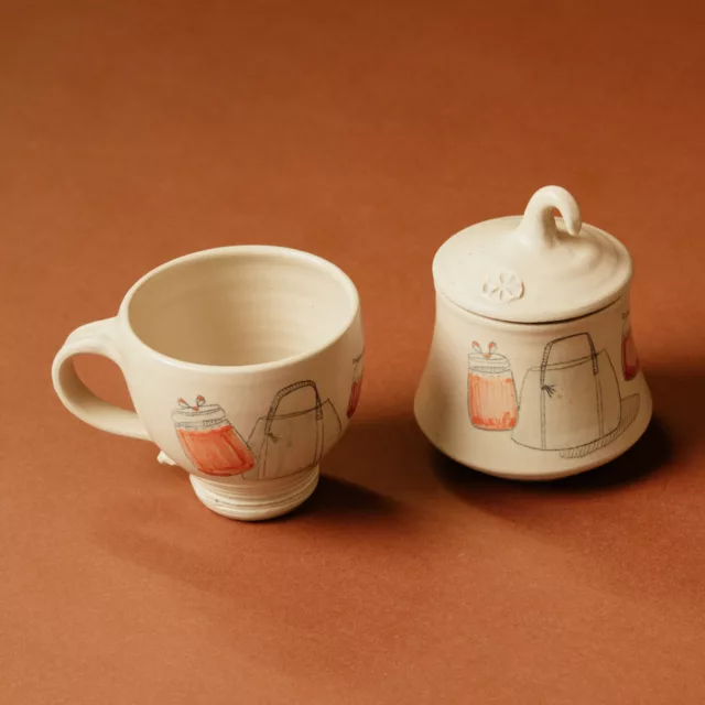 Pale ceramic cup and lidded pot with a line-drawn design picked out in orange, bespoke lifestyle piece