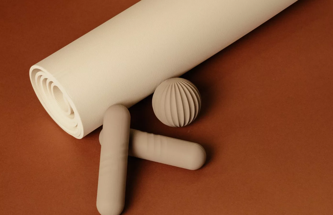 Rolled yoga mat, massage ball and roller in cream on a terracotta ground, bespoke wellbeing and sport accessories