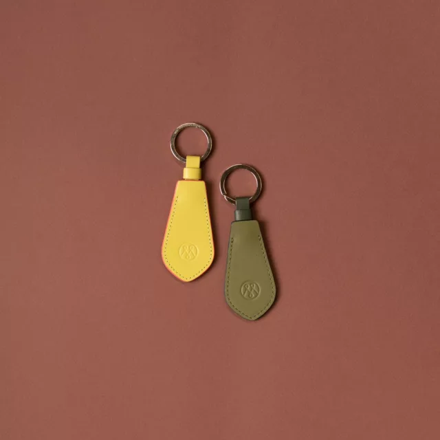 Two smooth leather keyrings in yellow and olive green, embossed with an emblem, Maison Maëstra