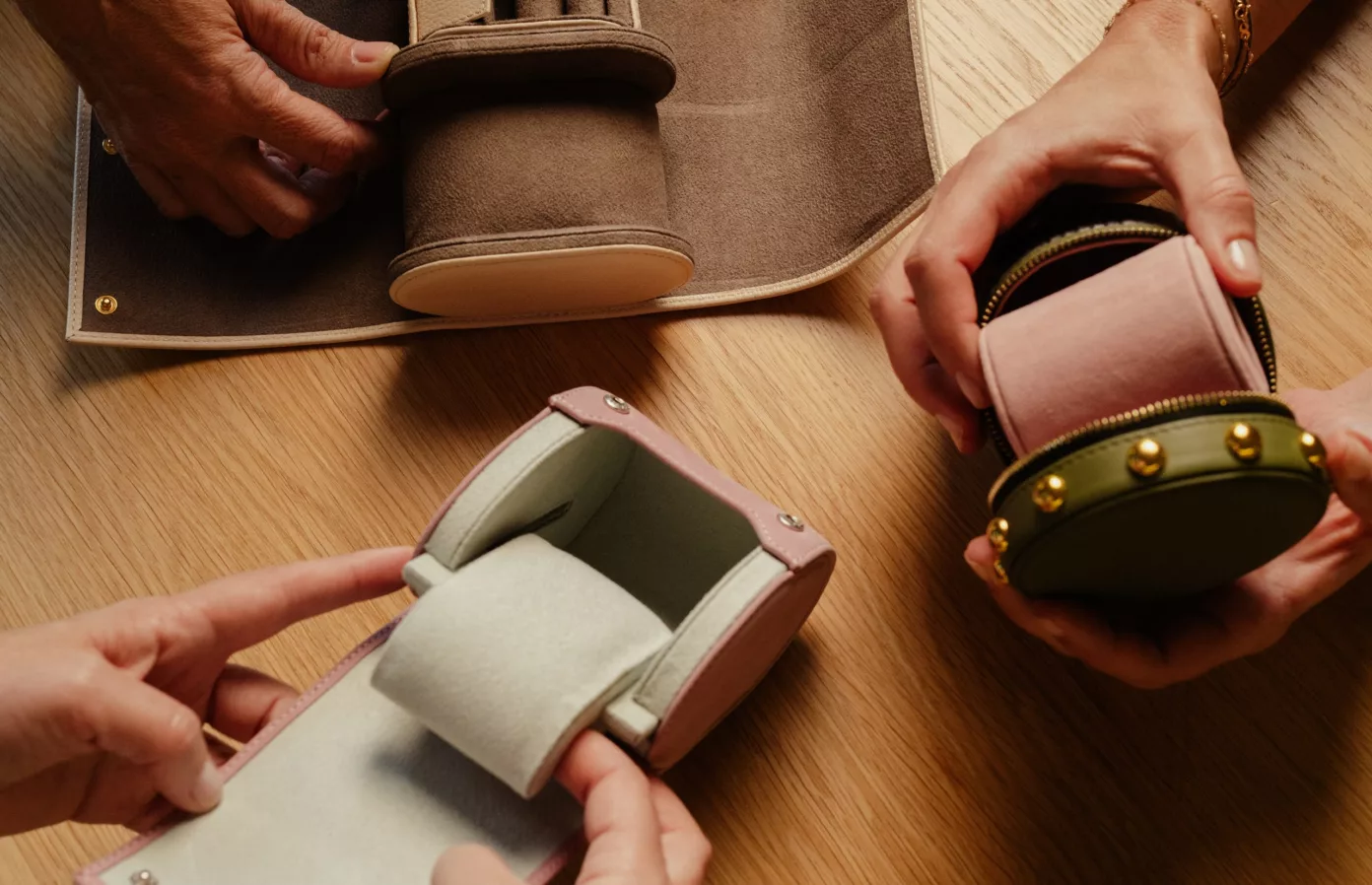 Mains ouvrant un rouleau en cuir taupe, un étui rose et un écrin rond clouté, écrins de voyage sur-mesure, Maison Maëstra
