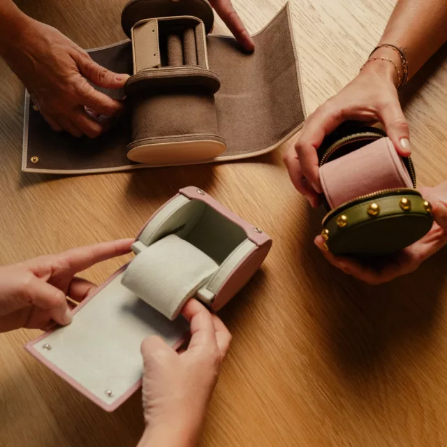 Mains dépliant un rouleau en cuir taupe et ouvrant un étui rose et un écrin rond clouté, écrins à bijoux souples