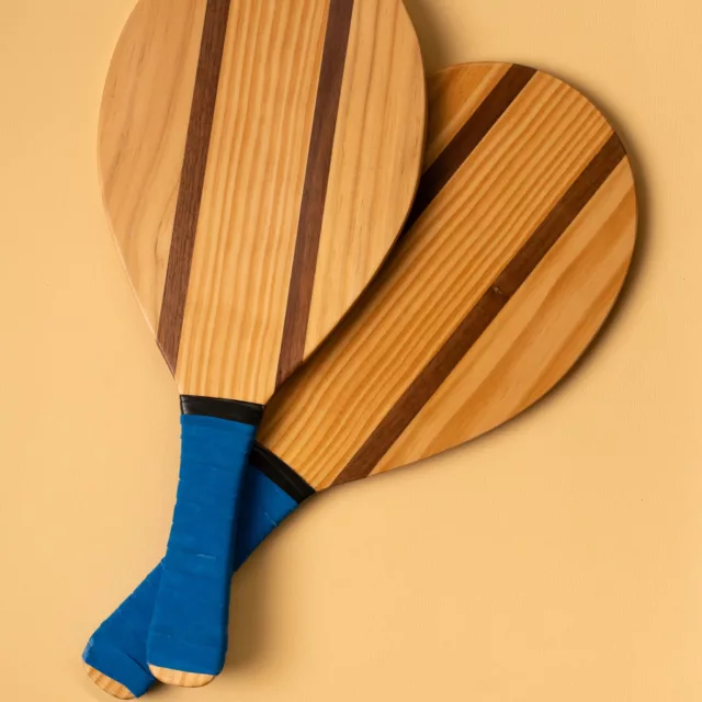 Deux raquettes de plage en bois clair à bandes sombres et manches bleus, jeu sur-mesure pour les familles